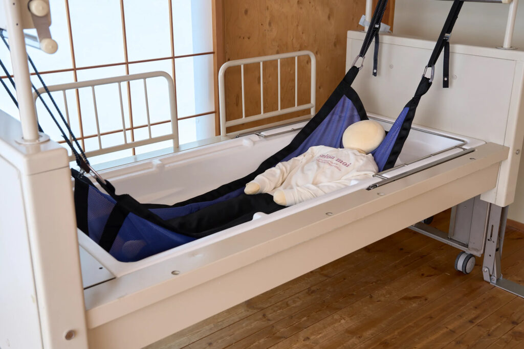 ハンモックに寝たままの姿勢で、せり上がった浴槽に入る様子